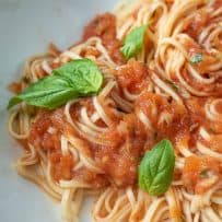 A closeup of roasted tomato sauce mixed with fresh linguine garnished with fresh basil leaves