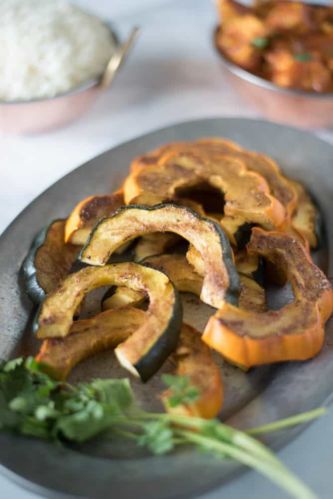 Horseshoe shaped slices of acorn squash coated with spices piled on a plate