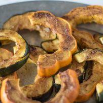 Orange and green skinned acorn squash. Sliced and sprinkled with Indian spices on a plate