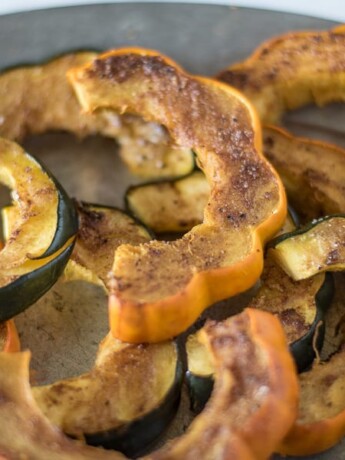 Orange and green skinned acorn squash. Sliced and sprinkled with Indian spices on a plate