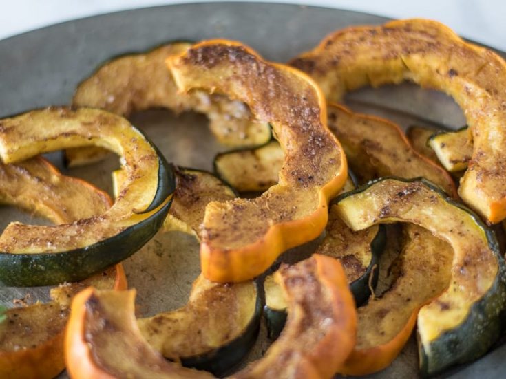 Orange and green skinned acorn squash. Sliced and sprinkled with Indian spices on a plate