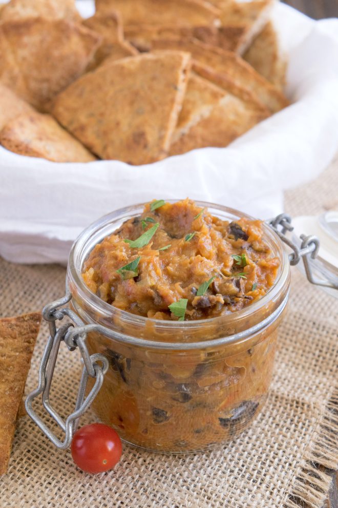 A jar filled with eggplant dip served with pita chips