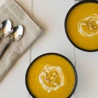 2 bowls of pumpkin and root vegetable soup viewed from overhead with 2 spoons and a linen napkin