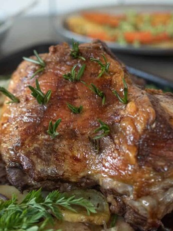 A perfectly browned, roasted leg of lamb in a roasting pan surrounded by vegetables