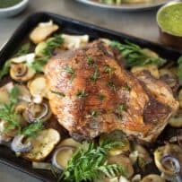A pan of sliced potatoes, fennel and onion in a roasting pan topped with roast lamb