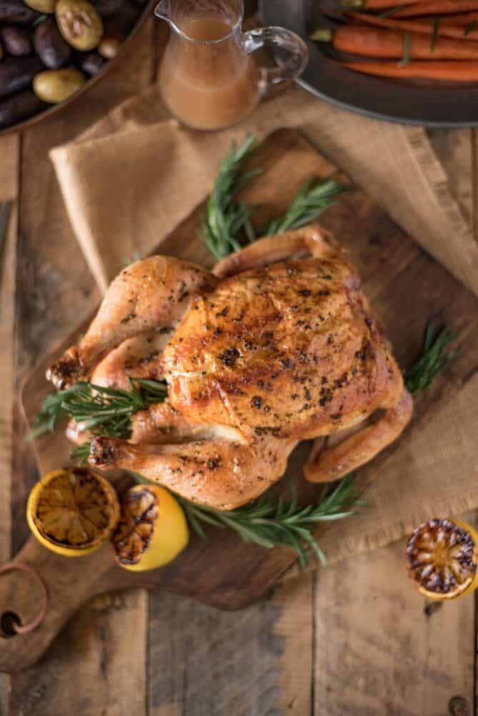 A whole roasted chicken viewed from overhead with lemon halves