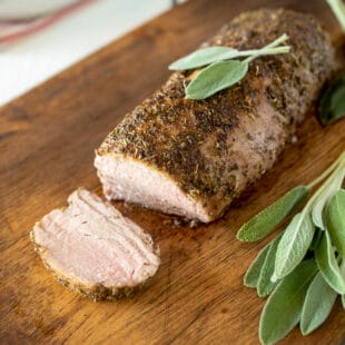 A closeup of sliced pork tenderloin surrounded by fresh sage leaves