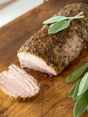 A closeup of sliced pork tenderloin surrounded by fresh sage leaves