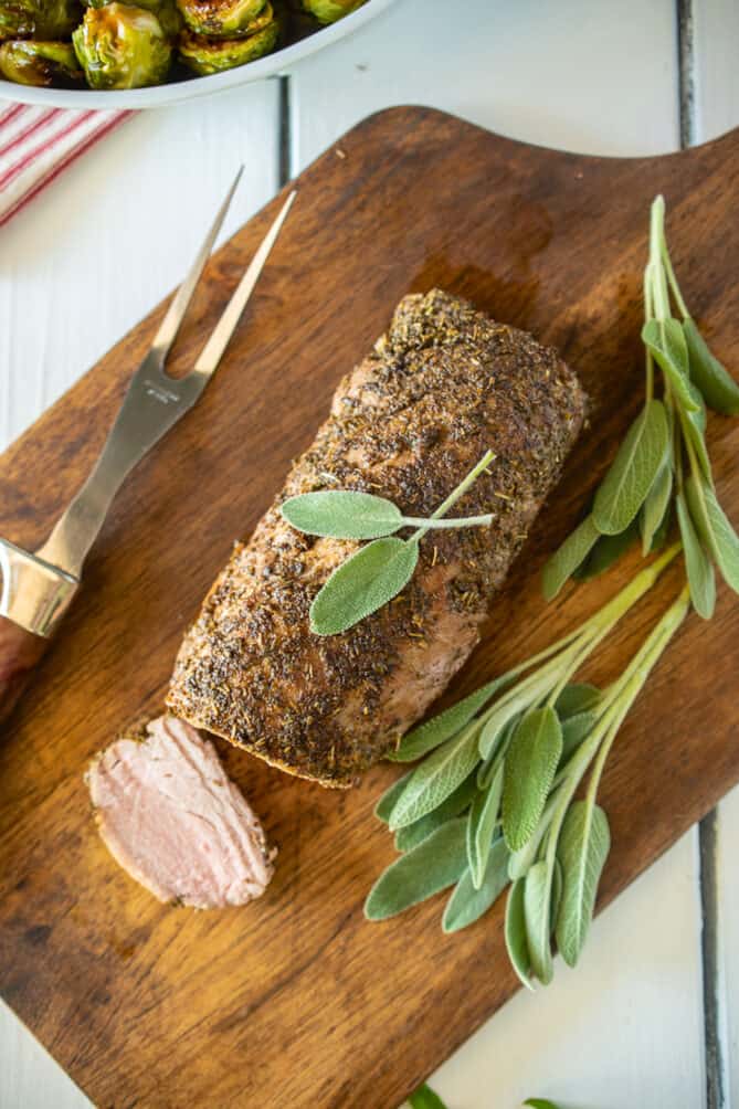 A pork tenderloin on a cutting board viewed from overheat with fresh sage leaves