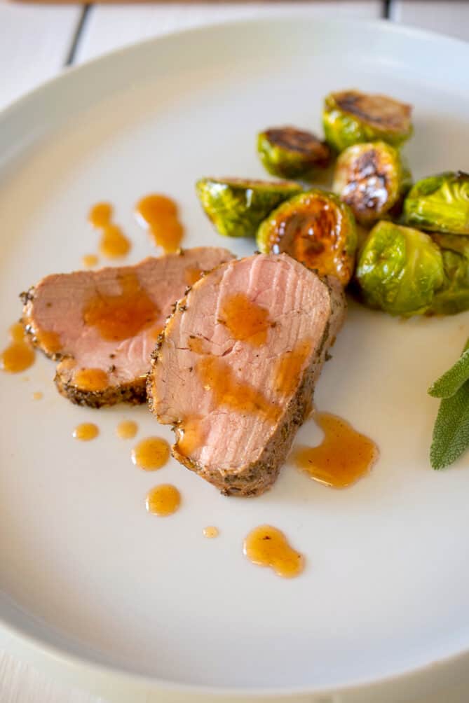 Sliced of pork on a white plate with Brussels sprouts and a cranberry glaze