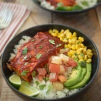 A filet of salmon on rice with avocado, salsa, corn and lime wedges