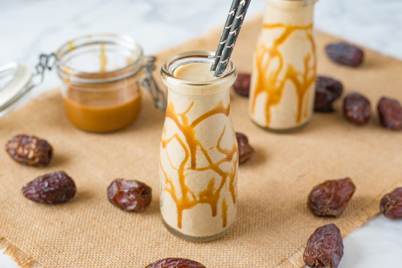 Salted caramel date shake in a glass bottle surrounded by dates and salted caramel