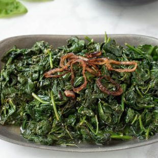 Sauteed spinach with crispy shallots in a grey bowl