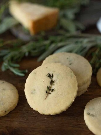 Herb and parmesan shortbread crackers displayed on a board with fresh herbs