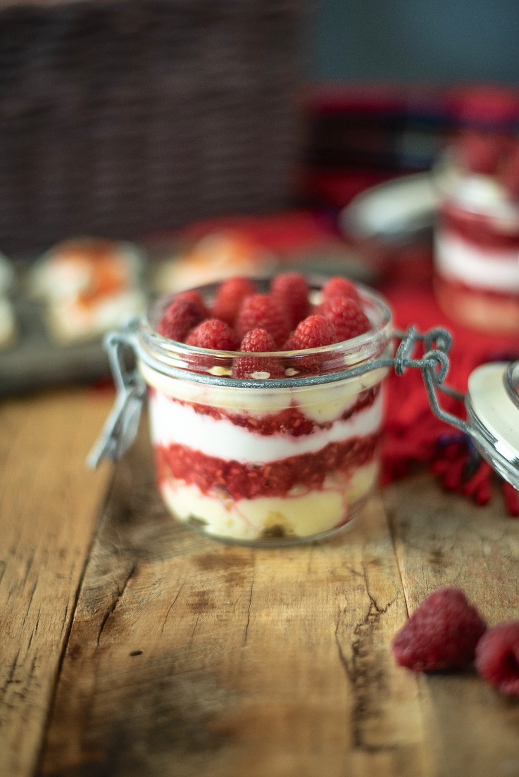 A side view showing the layers of custard, raspberry and cream through a glass jar