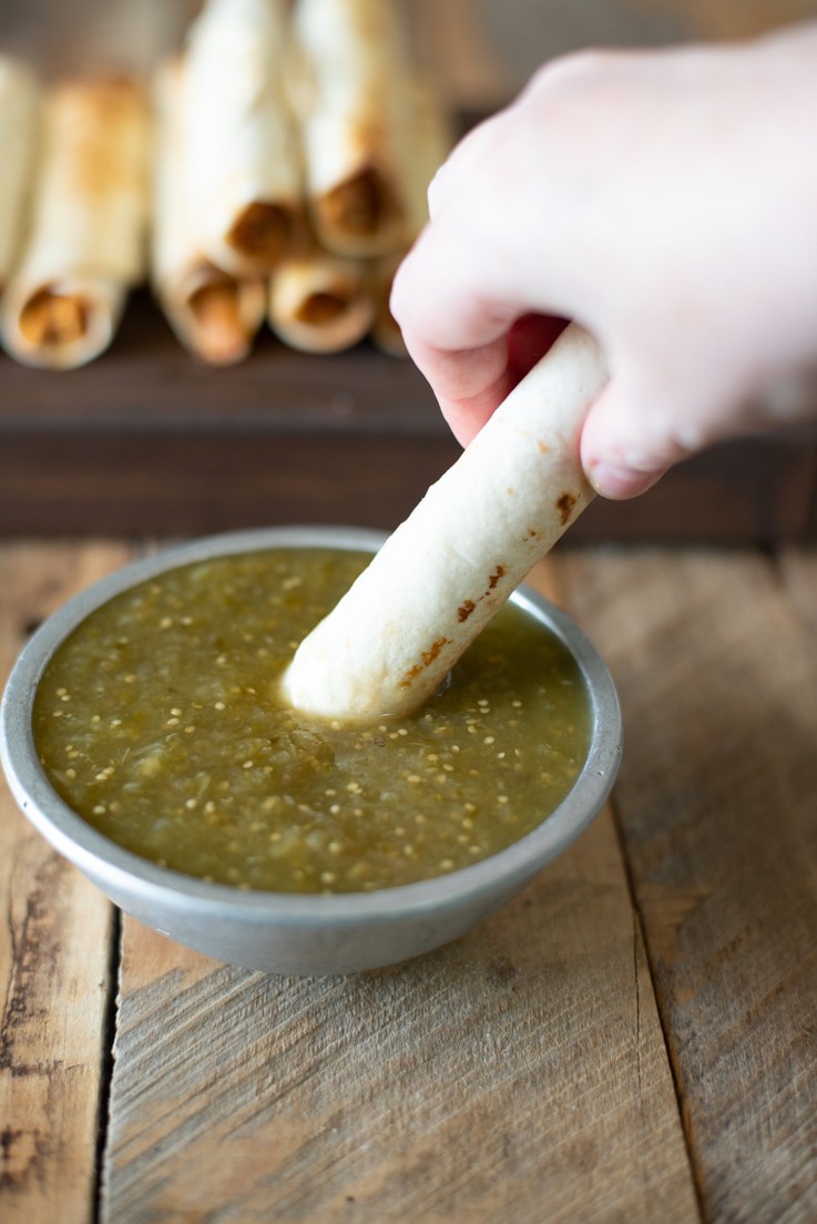 Dipping a shredded chicken baked taquito into a bowl of salsa verde