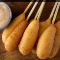 7 shrimp corn dogs on a wood serving board with lime wedges
