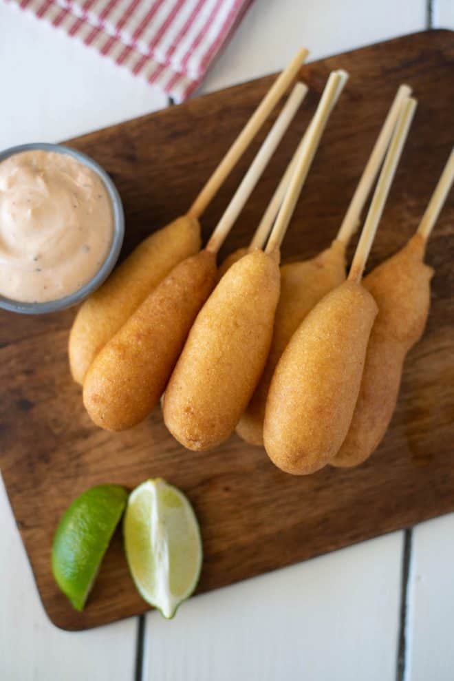 A stack of shrimp corn dogs on a serving board with dipping sauce viewed from overhead