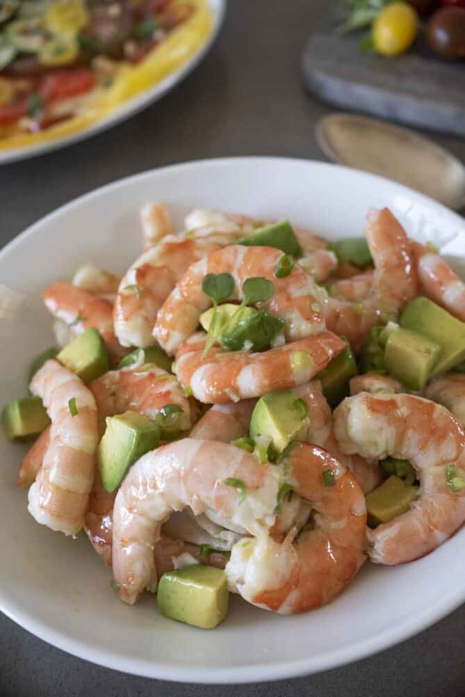 A closeup of cooked shrimp in a bowl mixed with chopped avocado and a simple dressing