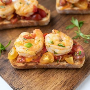 2 cooked shrimp on top of chopped tomatoes on a slice of crispy bread