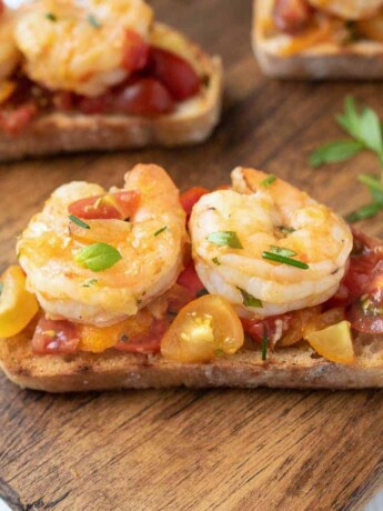 2 cooked shrimp on top of chopped tomatoes on a slice of crispy bread