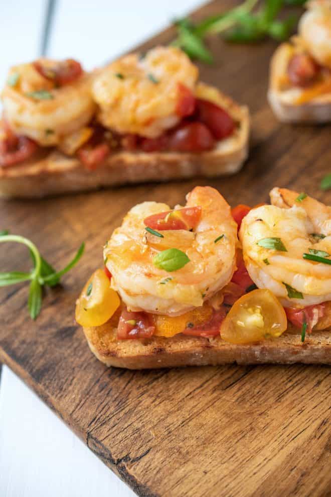 Grilled bread slices topped with shrimp and cherry tomatoes