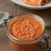 Sicilian tomato pesto sauce in a jar with a plate of pasta