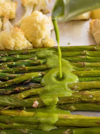 Drizzling a green herb sauce over fresh roasted asparagus and cauliflower