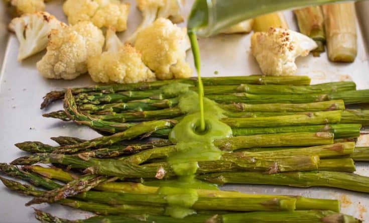 Drizzling a green herb sauce over fresh roasted asparagus and cauliflower