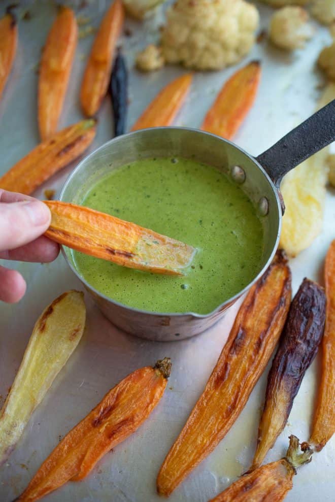 Dipping a roasted carrot into a vibrant green herb sauce