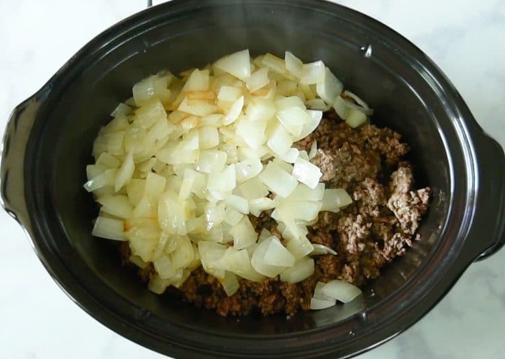 The softened onions and garlic are added to the slow cooker with the beef