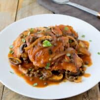 Chicken thighs cooked with mushrooms, capers and onions on a round white plate
