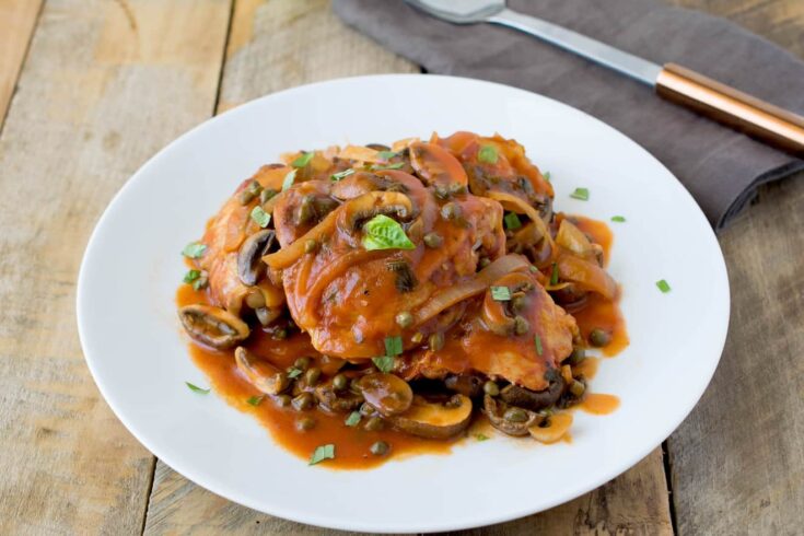 Chicken thighs cooked with mushrooms, capers and onions on a round white plate