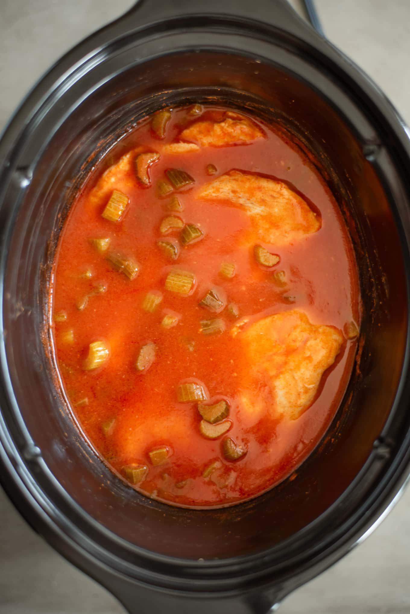 Chicken breasts cooking in buffalo sauce in a slow cooker