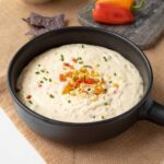 A cheesy corn and pepper dip in a black bowl