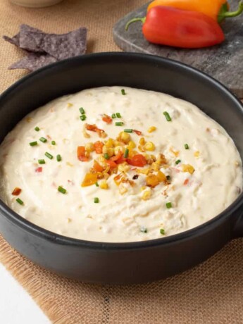 A cheesy corn and pepper dip in a black bowl