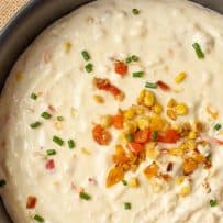 A closeup of corn and pepper cheese dip topped with corn, chives and peppers