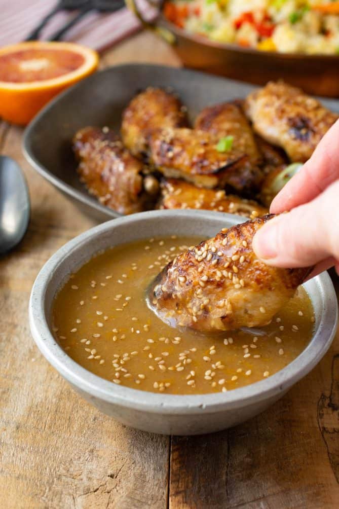 Dipping a chicken wing into orange sauce