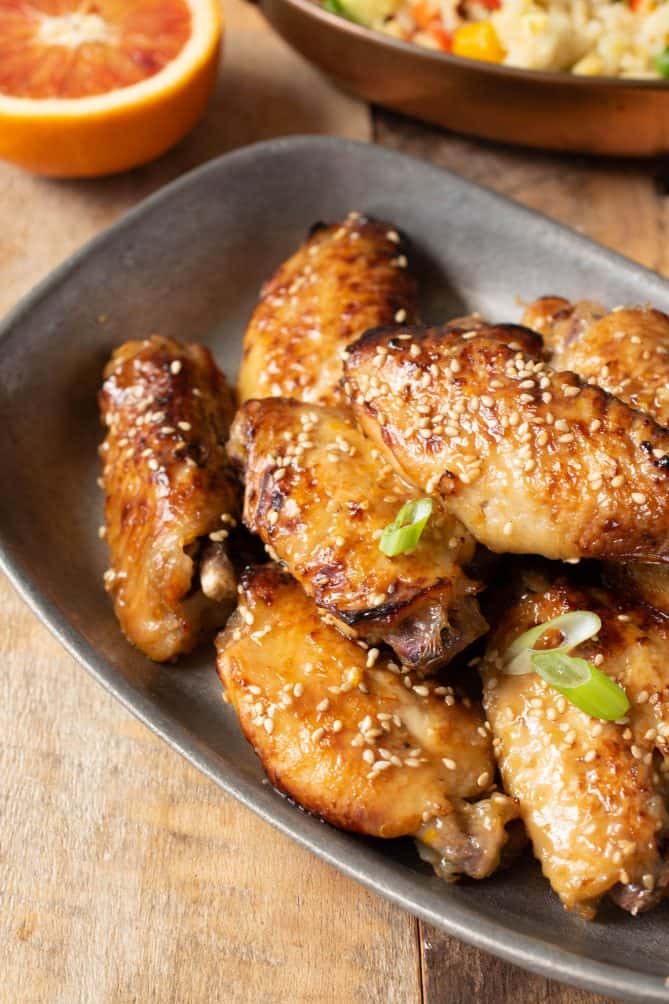 A closeup of an orange chicken wing sprinkled with sesame seeds