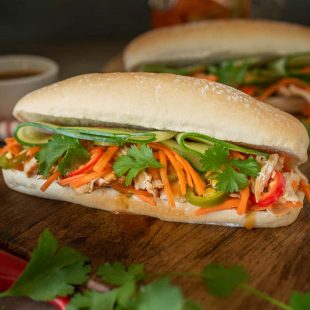 A soft roll is filled with shredded chicken, carrot slaw, cucumber and cilantro