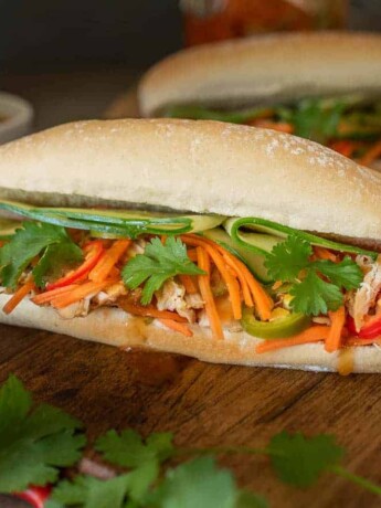 A soft roll is filled with shredded chicken, carrot slaw, cucumber and cilantro