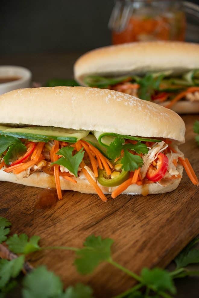 Shredded chicken, carrot slaw, cilantro and cucumber spilling out of a banh mi sandwich