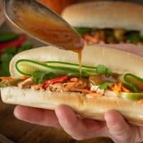 Holding a chicken banh mi while drizzling the most amazing sauce