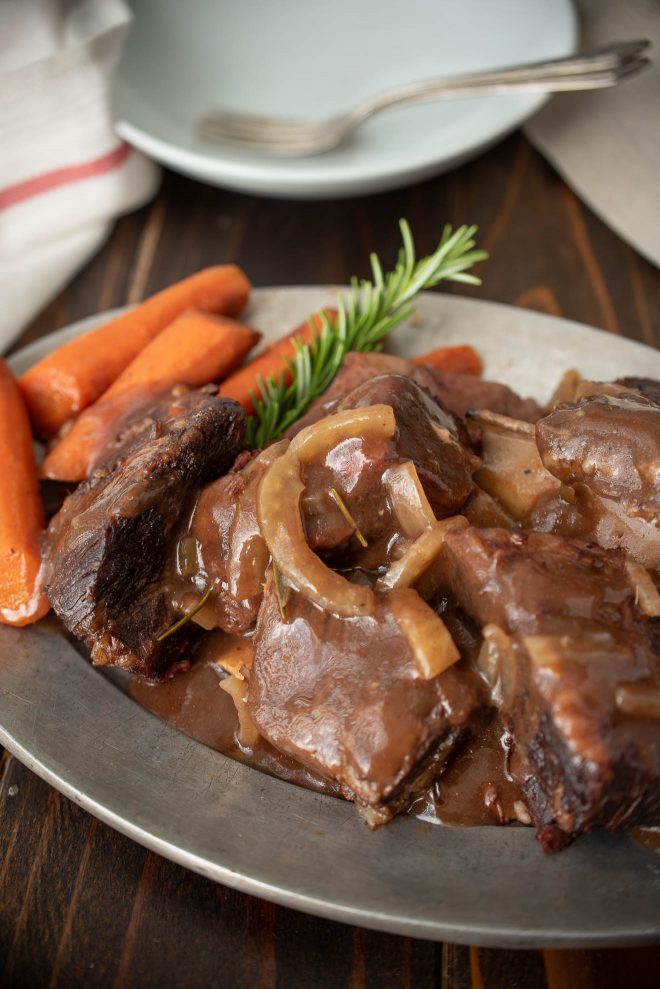 Short ribs and gravy on a plate with carrots and rosemary