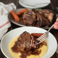 Beef short ribs on polenta with carrots on a white plate