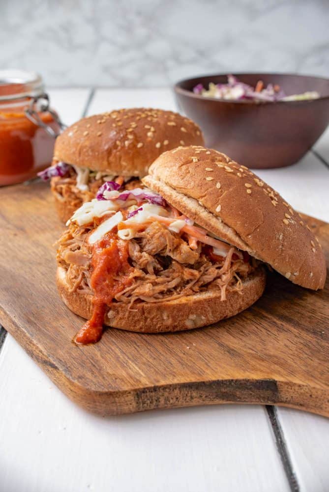 A pulled pork sandwich with the top of the bun at an angle showing the coleslaw and sauce