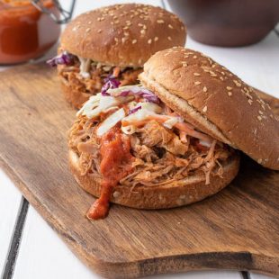 A pulled pork sandwich with the top bun tilted showing the meat topped with coleslaw