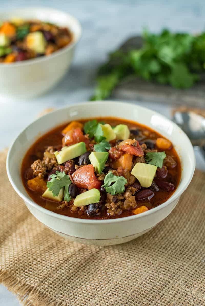 Slow cooker beef and sweet potato chili in a white bowl garnished with cilantro and avocado