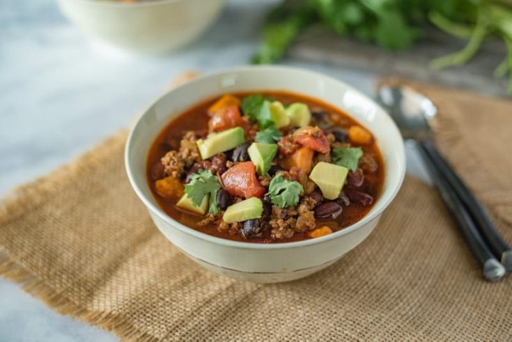 Slow cooker beef and sweet potato chili served in a white bowl with a spoon