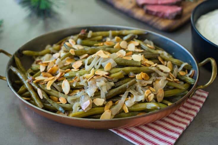 A copper serving dish filled with slow cooker green beans